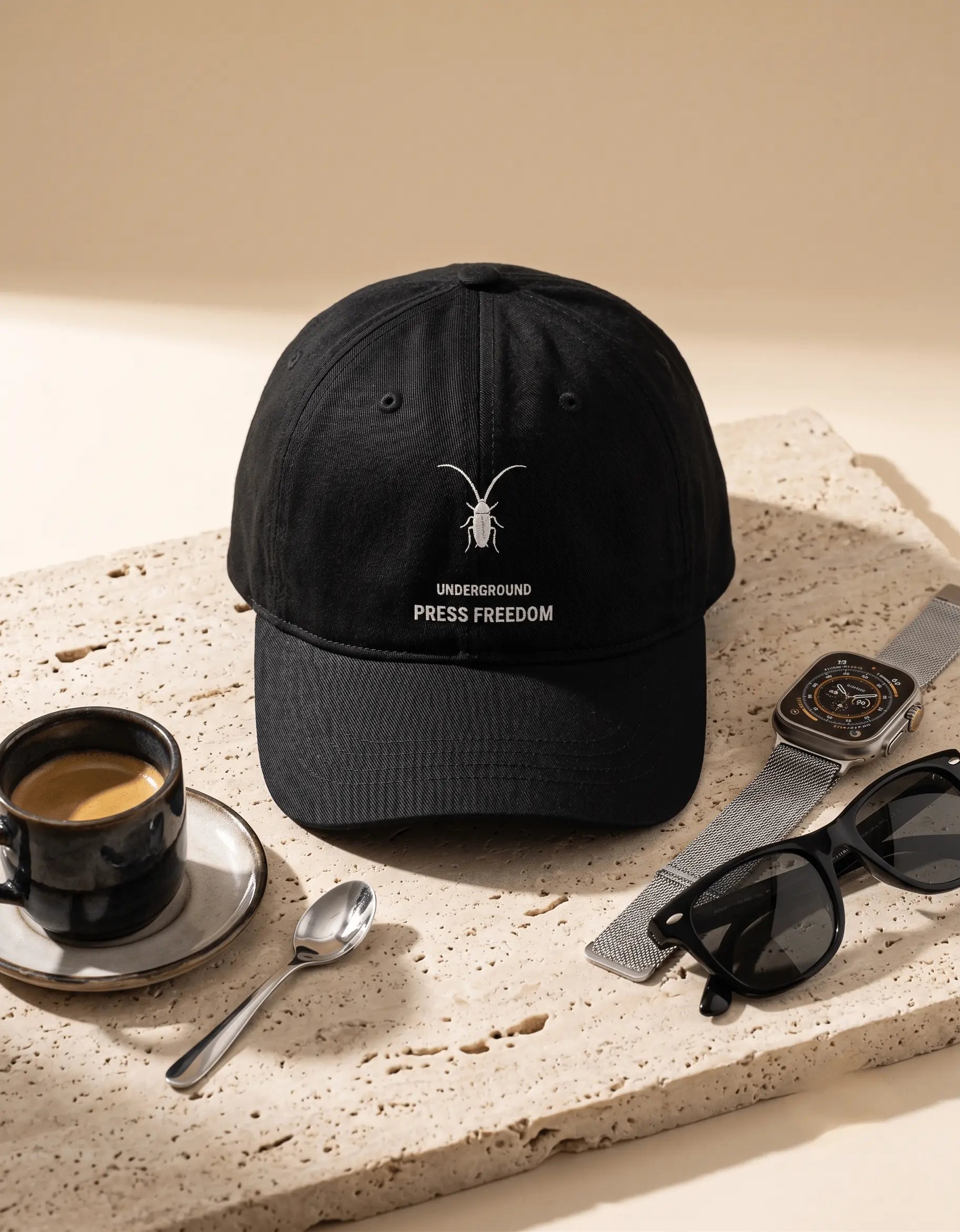 Premium black cotton drill baseball cap by Roach Resistance, part of the exclusive Press Freedom streetwear collection on beige background stone and sunglasses around.